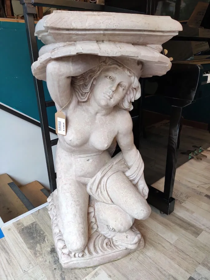 Statua in marmo raffigurante una donna che regge una mensola, scolpita in un unico blocco.
